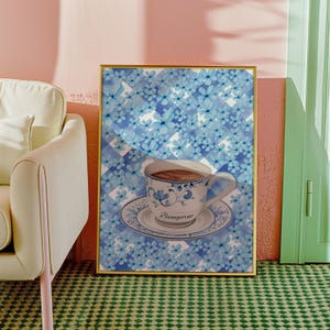 K&ouml;nnte beinhalten: Ein goldfarbener Druck mit einem blau-wei&szlig; karierten Hintergrund, auf dem eine blau-wei&szlig;e Teetasse mit dem Wort "Buongiorno" zu sehen ist. Die Teetasse steht auf einer wei&szlig;en Untertasse.