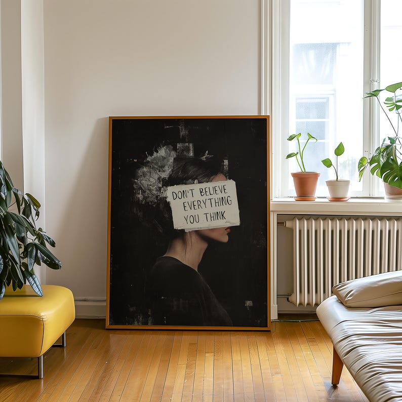 May include: A black and white art print featuring a woman's profile with a piece of paper covering her eyes. The paper has the text "Don't believe everything you think" written on it.