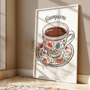 K&ouml;nnte beinhalten: Ein wei&szlig;er gerahmter Druck mit dem Text "Buongiorno" in schwarzer Schrift. Der Druck zeigt eine handgezeichnete Illustration einer Tasse und Untertasse mit einem floralen Muster. Die Tasse ist mit braunem Kaffee gef&uuml;llt.