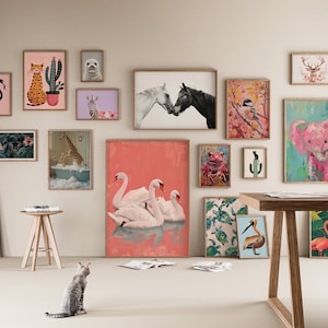 May include: A collection of framed animal illustrations in a variety of styles and colors, including a tiger, giraffe, elephant, flamingo, swan, and more. The illustrations are displayed on a white wall with a wooden table and a cat in the foreground.