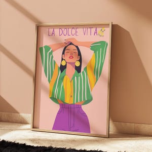 May include: Framed art print featuring a woman with arms raised, wearing a green and yellow striped shirt, purple pants, and lemon earrings. The text "LA DOLCE VITA" is at the top of the print.