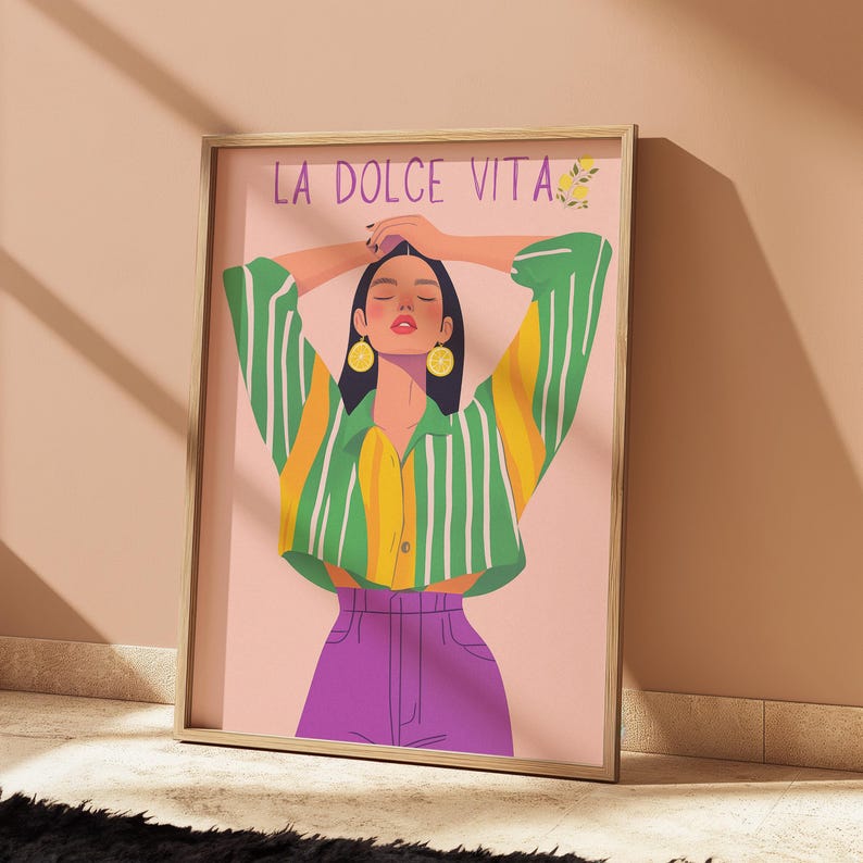 May include: Framed art print featuring a woman with arms raised, wearing a green and yellow striped shirt, purple pants, and lemon earrings. The text "LA DOLCE VITA" is at the top of the print.