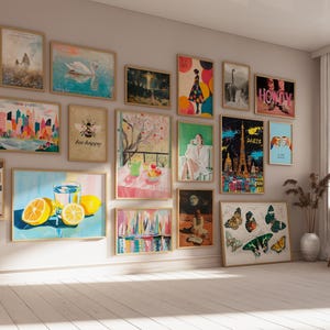May include: A gallery wall with a variety of framed prints, including a cityscape, a bee with the text "bee happy", a still life with fruit, a butterfly, and a lemon with a glass of water. The wall is painted a light beige color.