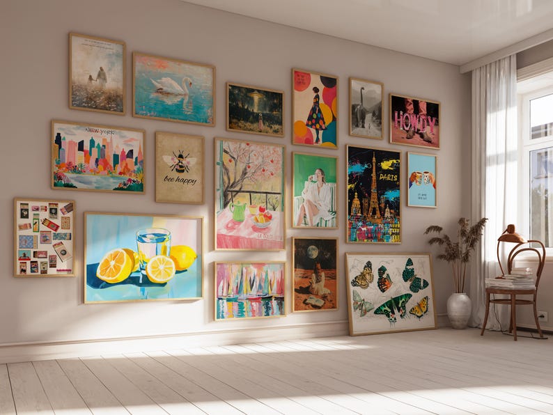 May include: A gallery wall with a variety of framed prints, including a cityscape, a bee with the text "bee happy", a still life with fruit, a butterfly, and a lemon with a glass of water. The wall is painted a light beige color.