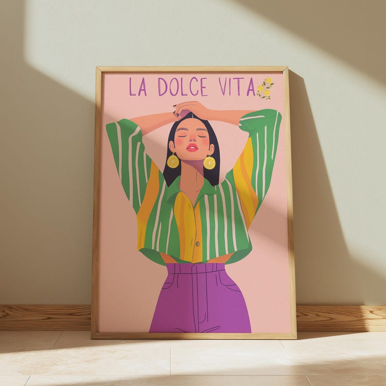 May include: A framed art print featuring a stylized illustration of a person with arms raised. The person wears a green and yellow striped shirt, purple pants, and lemon-shaped earrings. The words "LA DOLCE VITA" are at the top.