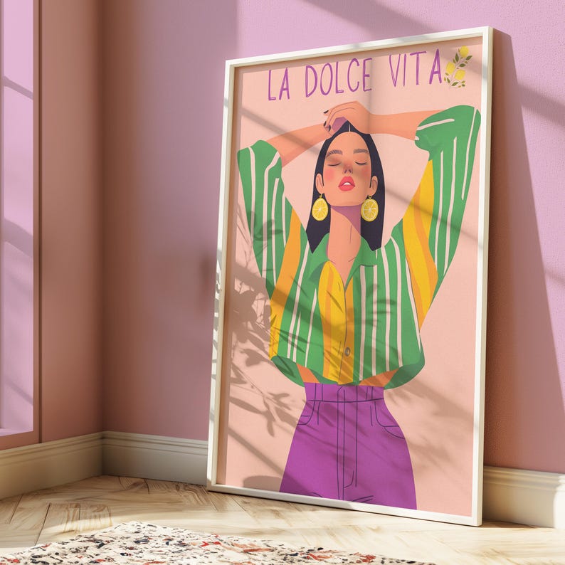 May include: A framed art print featuring a stylized illustration of a person with arms raised. The person wears a green and yellow striped shirt, purple pants, and lemon earrings. The words "LA DOLCE VITA" are at the top.
