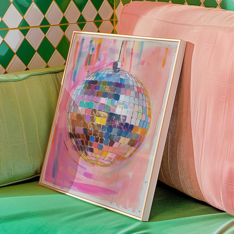 May include: A framed artwork depicting a disco ball with a multitude of colourful reflective squares, set against a pink and white painted backdrop. The frame has a gold finish. The artwork is leaning against a pink cushion.
