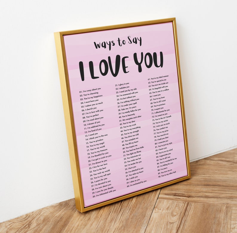May include: A pink and white printable poster with a gold frame. The poster has the text "Ways to Say I Love You" in black lettering. The poster lists 90 different ways to say "I love you" in black text on a pink and white background.