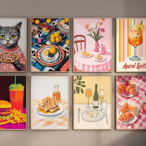May include: A set of nine framed prints featuring various food and drink illustrations. The prints are in a modern style with bright colors and bold lines. The prints include a cat eating pizza, a plate of waffles, a glass of Aperol Spritz, and a table setting with fruit and flowers.