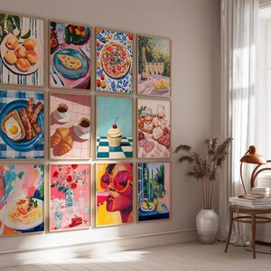 May include: A wall gallery featuring 12 framed prints of colorful, whimsical paintings depicting various food and drink items, including fruit, pizza, pastries, cocktails, and a cupcake. The prints are arranged in a grid pattern on a white wall.