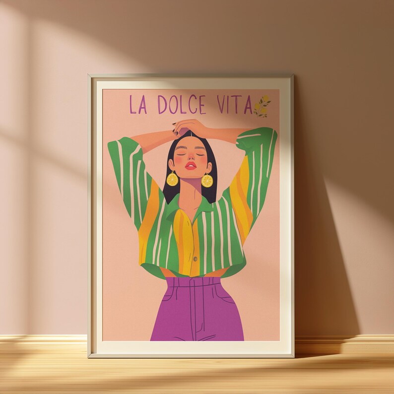 May include: Framed art print featuring a stylized illustration of a person with arms raised. The person wears a green and yellow striped shirt, purple pants, and gold earrings. The text "LA DOLCE VITA" is at the top.