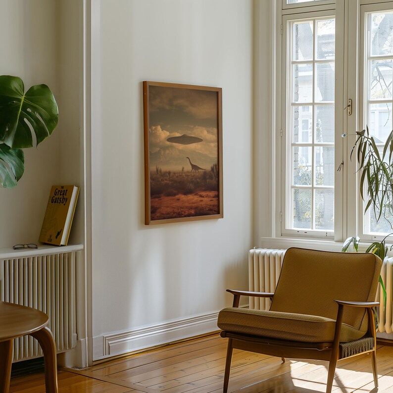 May include: A framed art print depicts a landscape with a dinosaur and a flying saucer in the sky. The artwork is in a wooden frame and hangs on a white wall. A mustard-colored armchair sits in front of a window.