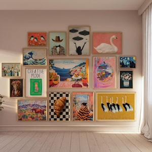 May include: A gallery wall with a variety of framed artwork, including a wave print, a cityscape, a swan, a disco ball, and a painting of birds. The wall is painted a light pink color and the frames are all in a similar style.