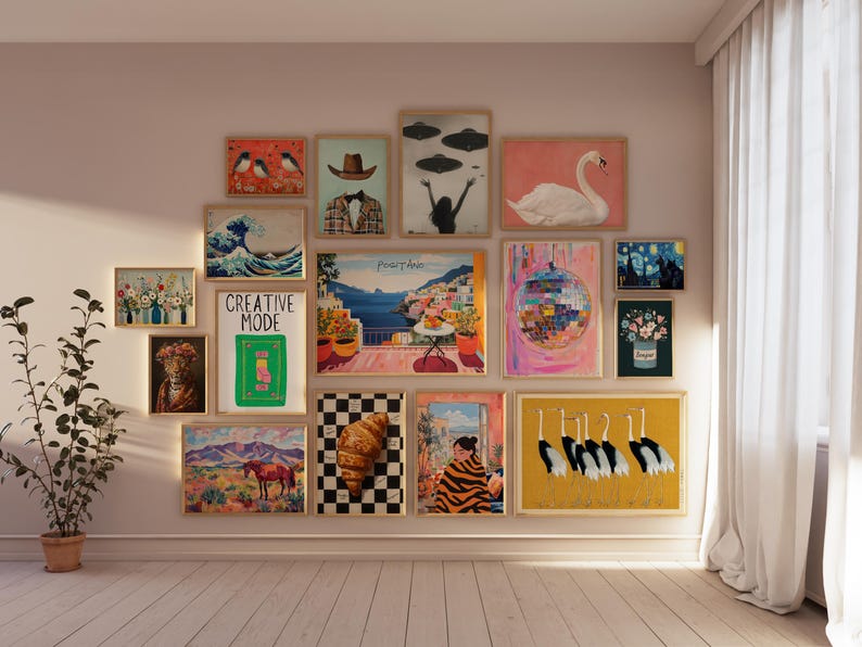 May include: A gallery wall with a variety of framed artwork, including a wave print, a cityscape, a swan, a disco ball, and a painting of birds. The wall is painted a light pink color and the frames are all in a similar style.