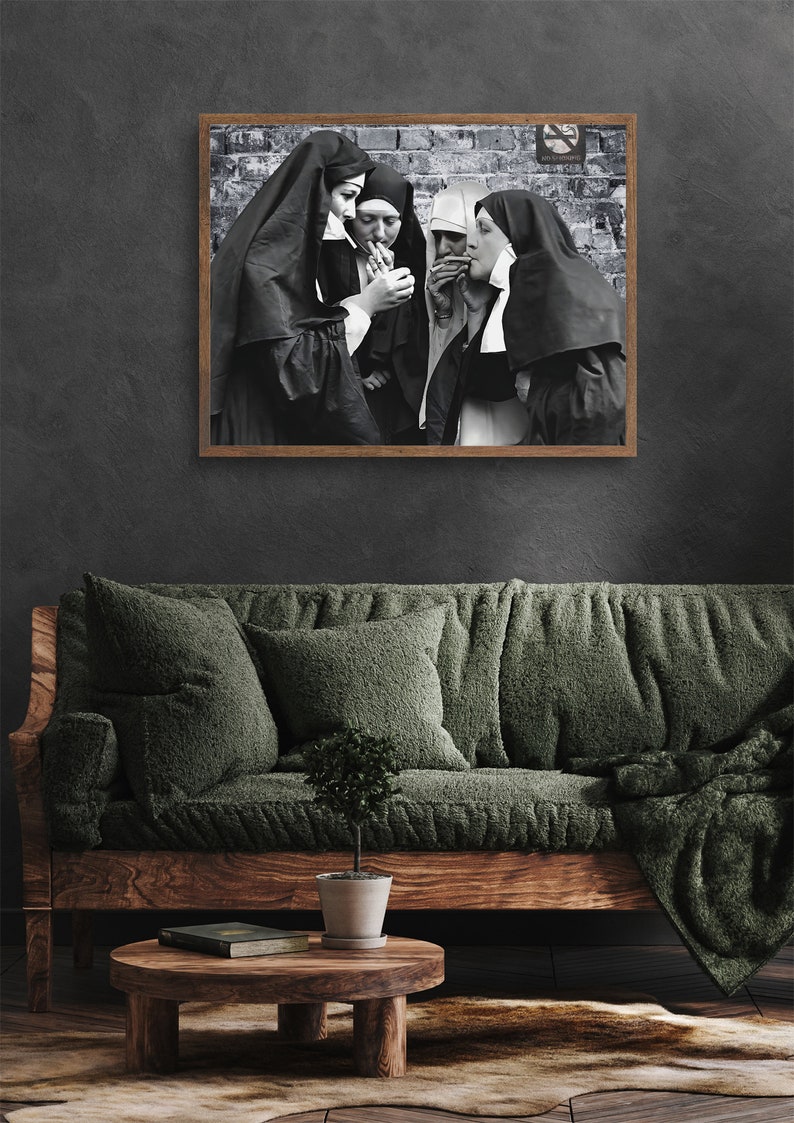May include: Black and white photograph of four nuns standing in front of a brick wall, each holding a cigarette. The photo is framed in a brown wooden frame.