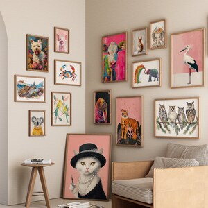 May include: A gallery wall with a variety of framed animal illustrations. The illustrations include a white dog, a pig, a crab, a koala, a cat, a tiger, a walrus, a cow, a bird, a group of owls, and a butterfly. The illustrations are framed in natural wood frames and are hung on a white wall.