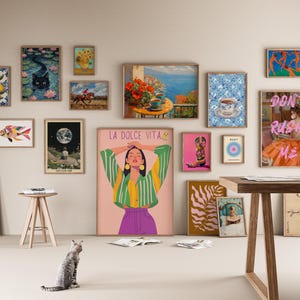 May include: A wall gallery featuring a variety of framed artwork, including a colorful fish, a woman with a green and yellow striped shirt, a cat, a moon, and a woman in a pink dress with the text "Don't Rush Me".