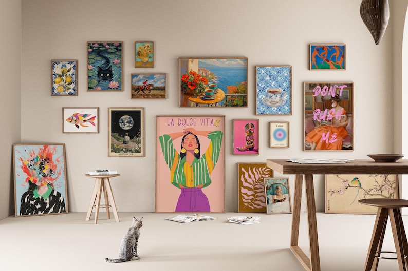 May include: A wall gallery featuring a variety of framed artwork, including a colorful fish, a woman with a green and yellow striped shirt, a cat, a moon, and a woman in a pink dress with the text "Don't Rush Me".