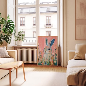 May include: A colorful painting of a rabbit with blue eyes and pink ears surrounded by flowers on a pink background.