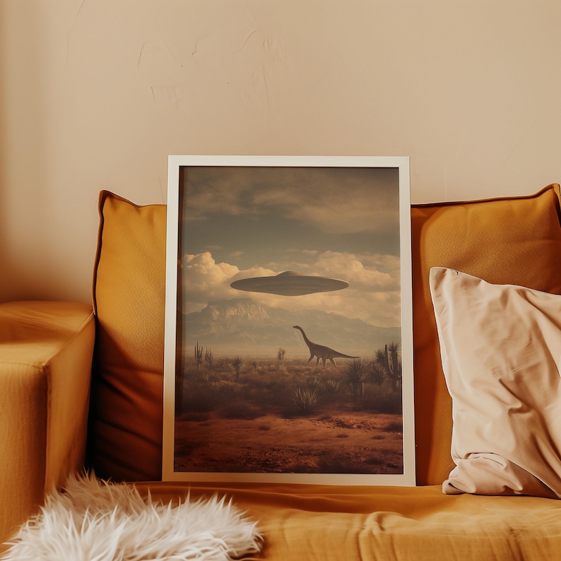 May include: A framed art print featuring a surreal landscape with a dinosaur and a UFO hovering in the sky. The artwork has a vintage aesthetic with a color palette of browns, tans, and blues. The print is displayed on a mustard-colored couch.