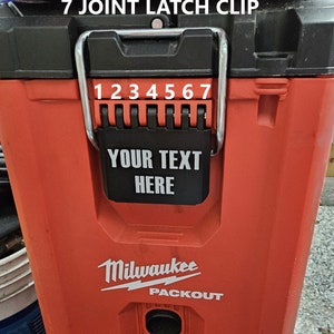 May include: A red Milwaukee Packout storage container with a black latch. The latch has the text "YOUR TEXT HERE" and the words "7 JOINT LATCH CLIP" above it. The numbers 1 through 7 are visible on the latch.