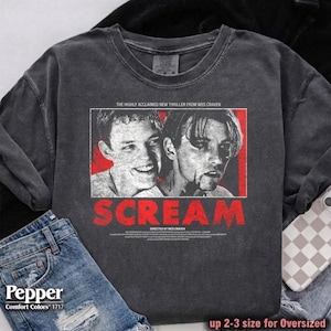 May include: Dark gray sweatshirt featuring a graphic from the movie "Scream." The design includes two faces, the title "SCREAM" in red, and text that reads "THE HIGHLY ACCLAIMED NEW THRILLER FROM WES CRAVEN." The sweatshirt is paired with denim shorts.