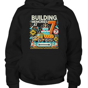 May include: Black hoodie with a graphic of a yellow dump truck carrying a birthday cake with the number 7 on it. The text "Building Memories at 7" is above the truck. There are traffic cones and road signs around the truck.