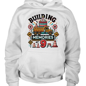 May include: White hoodie with a construction-themed birthday design. It features a cartoon dump truck with a birthday cake on the back, and the text "Building Memories at 9".