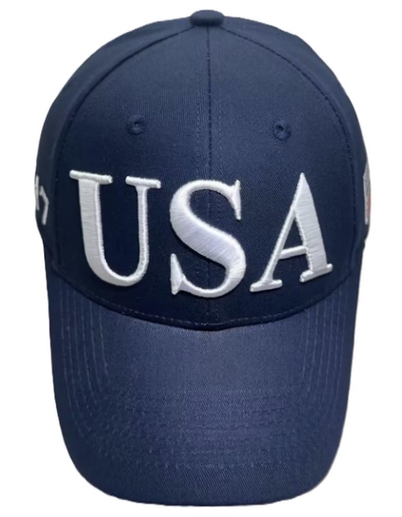 May include: Navy blue baseball cap with the word "USA" in white, bold, raised lettering across the front. The cap has a curved brim and a button on top. The cap is a solid color with a structured fit.