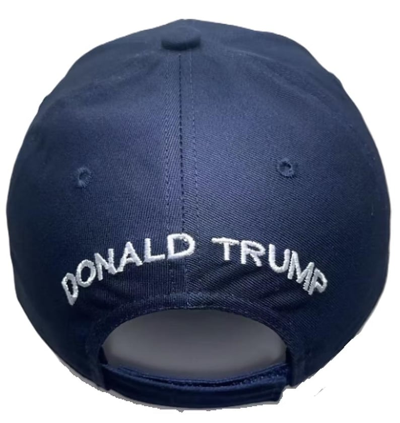 May include: A navy blue baseball cap with the embroidered text "DONALD TRUMP" in white across the back. The cap has a curved brim and a button on top.