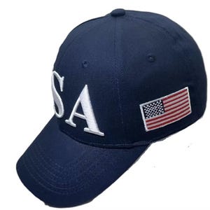 May include: A navy blue baseball cap with the white letters "USA" embroidered on the front. A small American flag patch is on the side. The cap has a curved brim and a button on top.