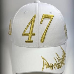 May include: White baseball cap with gold embroidered "47" on the front. The cap features additional gold embroidery on the side and brim, with a curved design. A classic, sporty accessory.