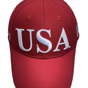 May include: A red baseball cap with the word "USA" embroidered in white across the front. The cap has a curved brim and a button on top.