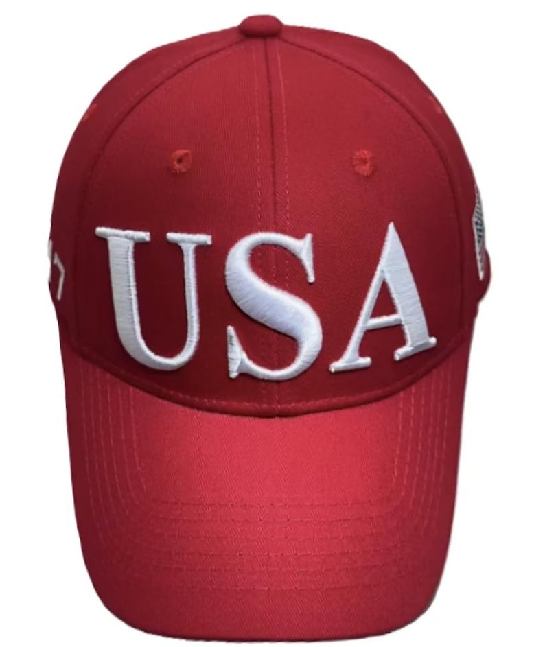 May include: A red baseball cap with the word "USA" embroidered in white across the front. The cap has a curved brim and a button on top.