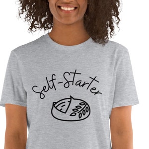Könnte beinhalten: Ein graues T-Shirt mit einer schwarzen Grafik eines Brotlaibs mit dem Text "Self-Starter" darüber.