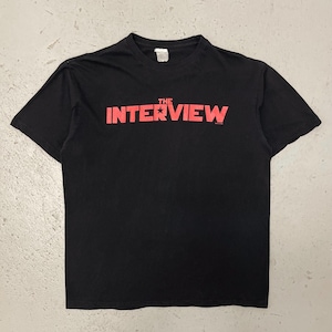 Peut inclure: T-shirt noir avec l'inscription rouge "THE INTERVIEW" sur la poitrine. Le texte est en gras, en police sans-serif. Le t-shirt est à col rond et à manches courtes.