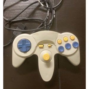 May include: A light gray video game controller with a black cable. The controller has a blue directional pad, yellow and blue buttons, and a yellow joystick. The Start button is visible.