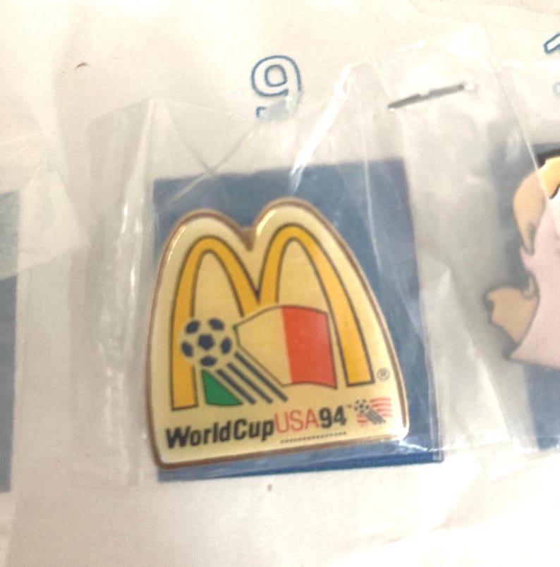 Puede incluir: Pin con el logotipo de los arcos dorados de McDonald's, un bal&oacute;n de f&uacute;tbol y un dise&ntilde;o de bandera. El pin es para la Copa del Mundo USA 94. El pin est&aacute; en una bolsa de pl&aacute;stico transparente.