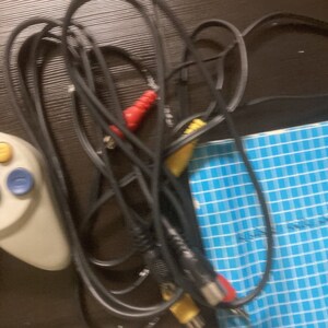 May include: A tangled black AV cable with red and yellow connectors. A white game controller with blue and yellow buttons is visible on the left. A blue and white checkered pattern is visible in the background.