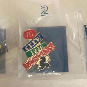 Puede incluir: Un pin con el logotipo de McDonald's y las palabras "CREW 1996 MONOPOLY" con un personaje del juego Monopoly. El pin est&aacute; en una bolsa de pl&aacute;stico sobre un fondo azul.