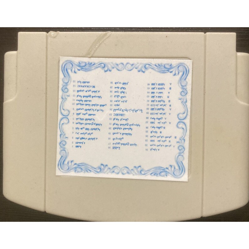 May include: A light gray rectangular cartridge with a white label featuring blue text and a decorative border. The label appears to list various items. The cartridge has a slightly textured surface.