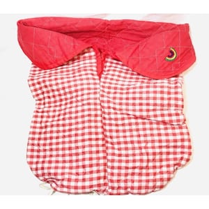 Pode incluir: Um porta-bebés acolchoado em tecido xadrez vichy vermelho e branco. A parte superior é vermelha lisa com um padrão acolchoado e um pequeno desenho bordado. O porta-bebés foi concebido para envolver um bebé.