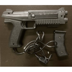 May include: Black plastic video game gun controller with the text "LETHAL ENFORCERS" on the side. Includes a separate grip and a wired connection. The controller has a textured grip and a trigger.