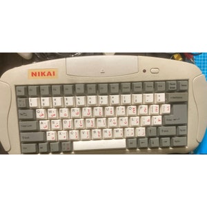 May include: A beige NIKAI keyboard with Arabic and English characters. The keyboard has a standard layout with function keys, number keys, and arrow keys. The keyboard has a power button and LED indicator.