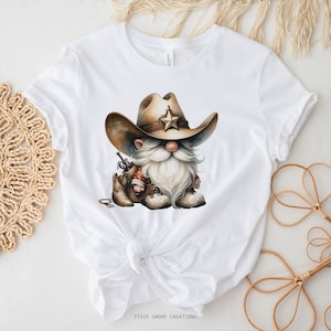 May include: White t-shirt with a cartoon image of a gnome wearing a cowboy hat with a star on it. The gnome is holding a gun and wearing boots. The text "PIXIE GNOME CREATIONS" is at the bottom of the shirt.