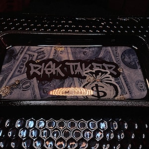 May include: Black tray with a money print design and gold accents. The tray has the words "Risk Taker" written in white letters on a black background. A money bag with a dollar sign is in the center of the tray.