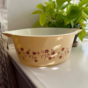May include: A yellow ceramic baking dish with a floral design in brown. The dish has a rounded shape and two handles.