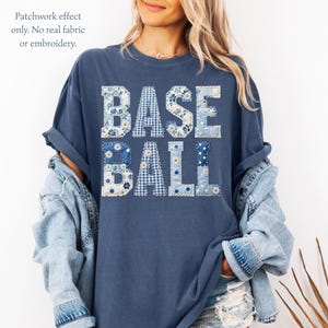 May include: A navy blue t-shirt with the word "BASEBALL" in a patchwork design. The letters are made of various blue and white floral and gingham patterns. The shirt has rolled-up sleeves and a relaxed fit.