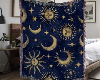 May include: A navy blue woven throw blanket with a gold celestial pattern featuring suns, moons, and stars. The blanket has a fringe border.