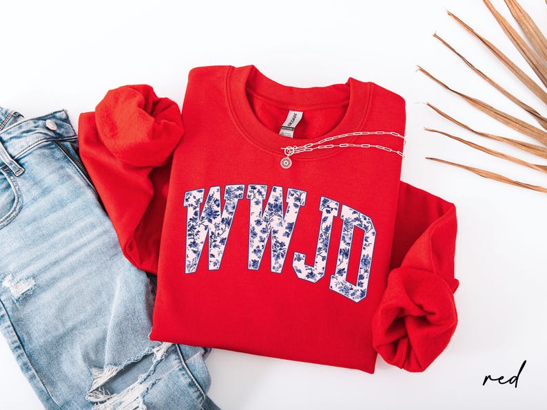 May include: A red sweatshirt with the letters "WWJD" in a floral design. The sweatshirt is paired with blue jeans and a silver necklace. The word "red" is written in the bottom right corner.